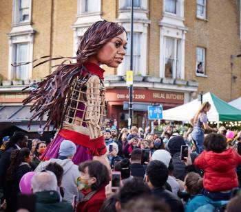 The Little Amal sculpture/puppet/costume on a city street, surrounded by crowds