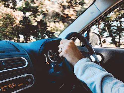 View from inside a car, of a person with their hands on the steering wheel