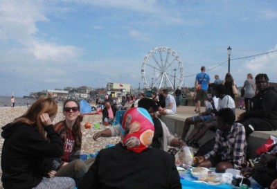 A group sitting on a beach having fun, with a funfair in the background