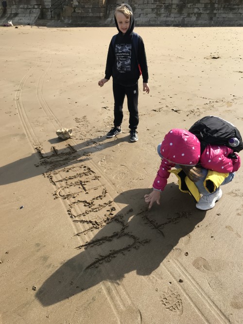 Two children playing on a beach, writing 'Ukraine' in the sand
